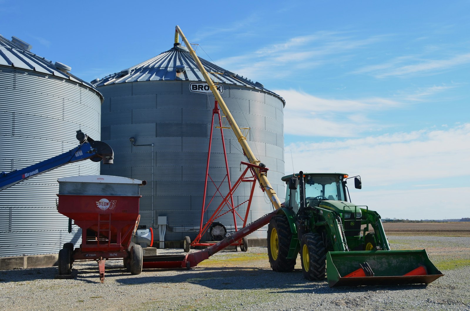 Tractor and grain auger next to farm silos