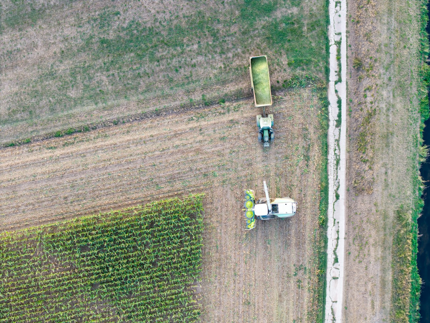 Aerial view of a harvester unloading grain into a truck beside the field